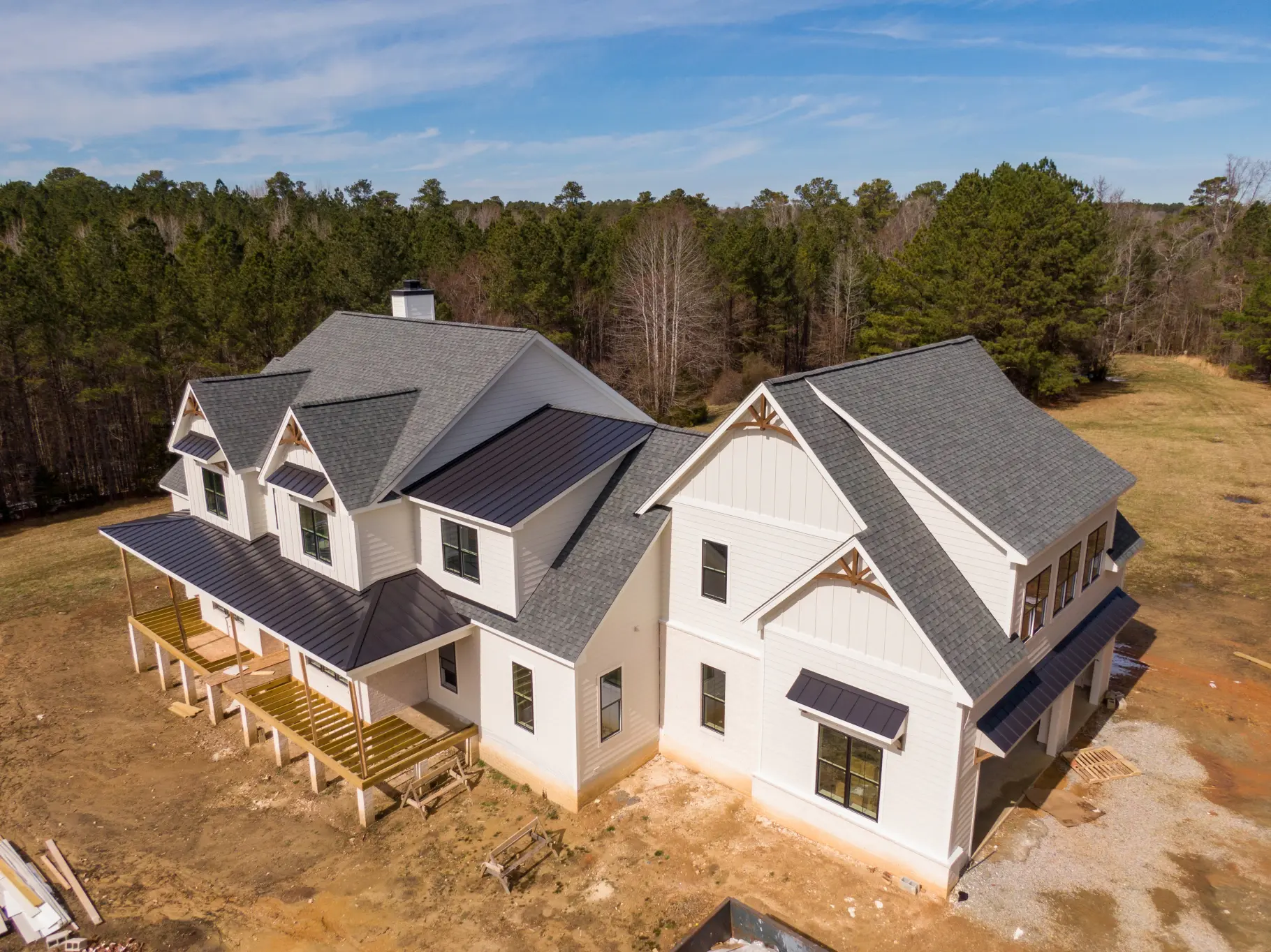 Aerial view of a large white farmhouse with shingle and standing-seam metal roofing