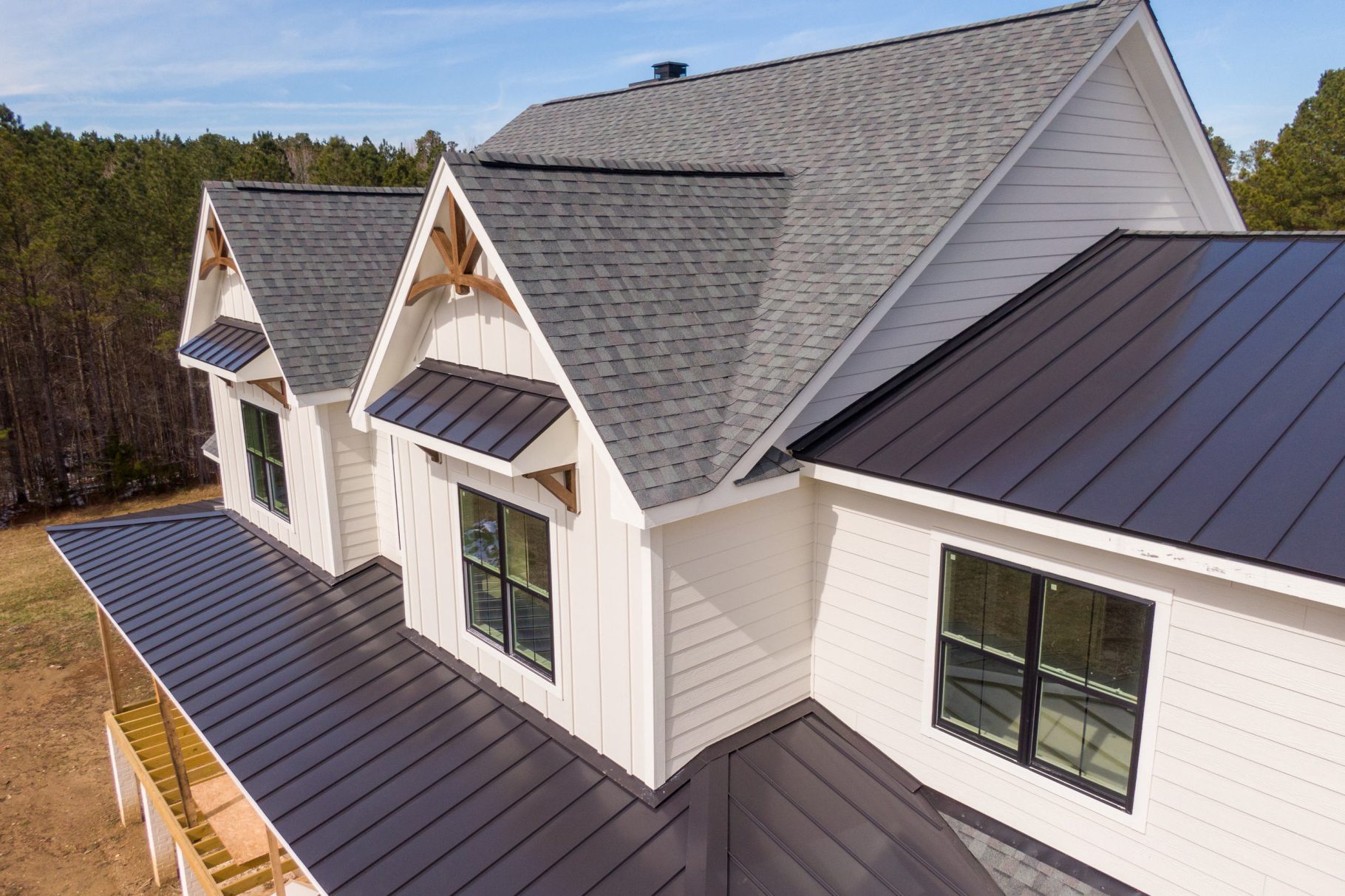 Close aerial view of dormers, shingles and standing-seam metal roofing on a white farmhouse