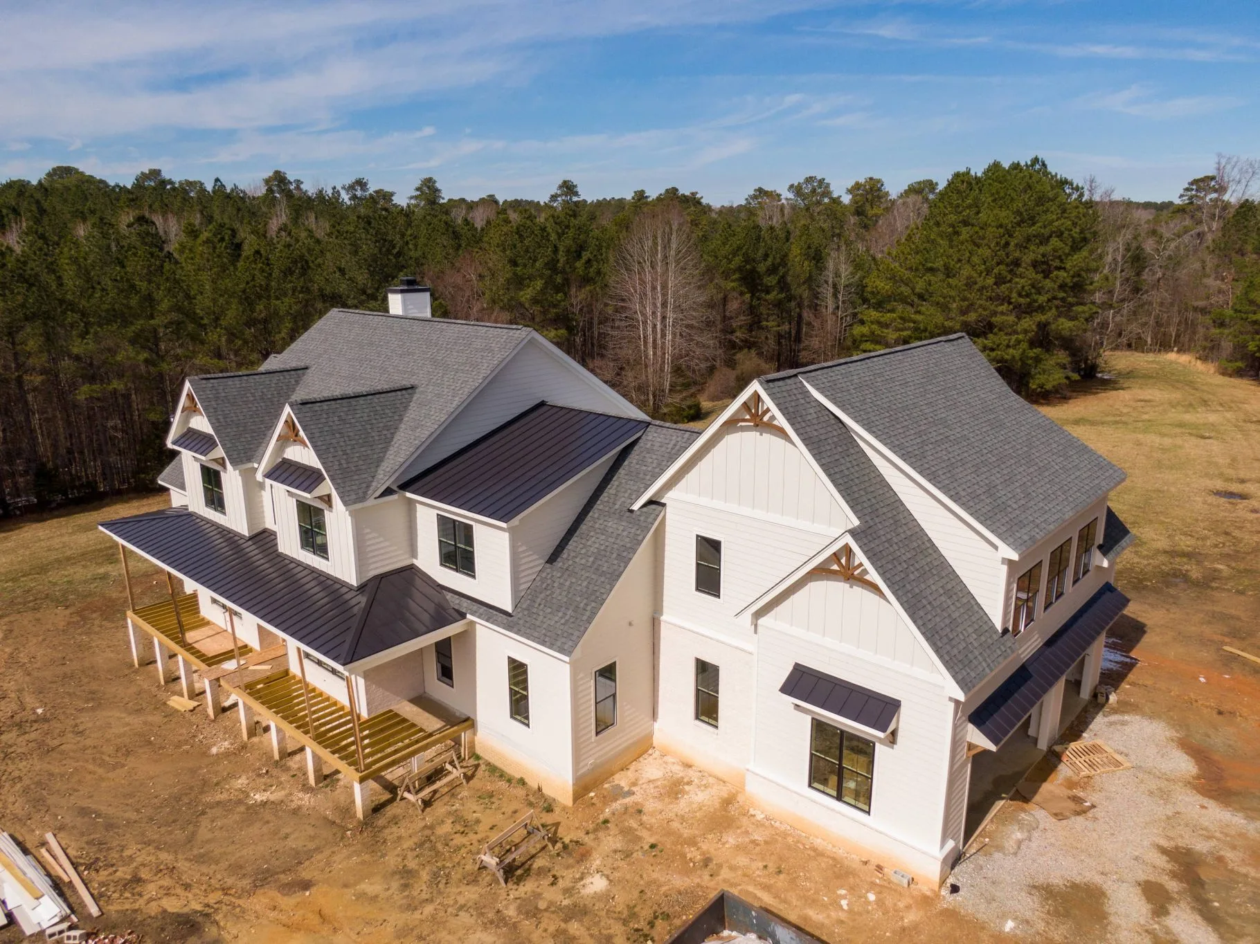 Aerial view of a newly built white farmhouse with a standing-seam metal and shingle roof