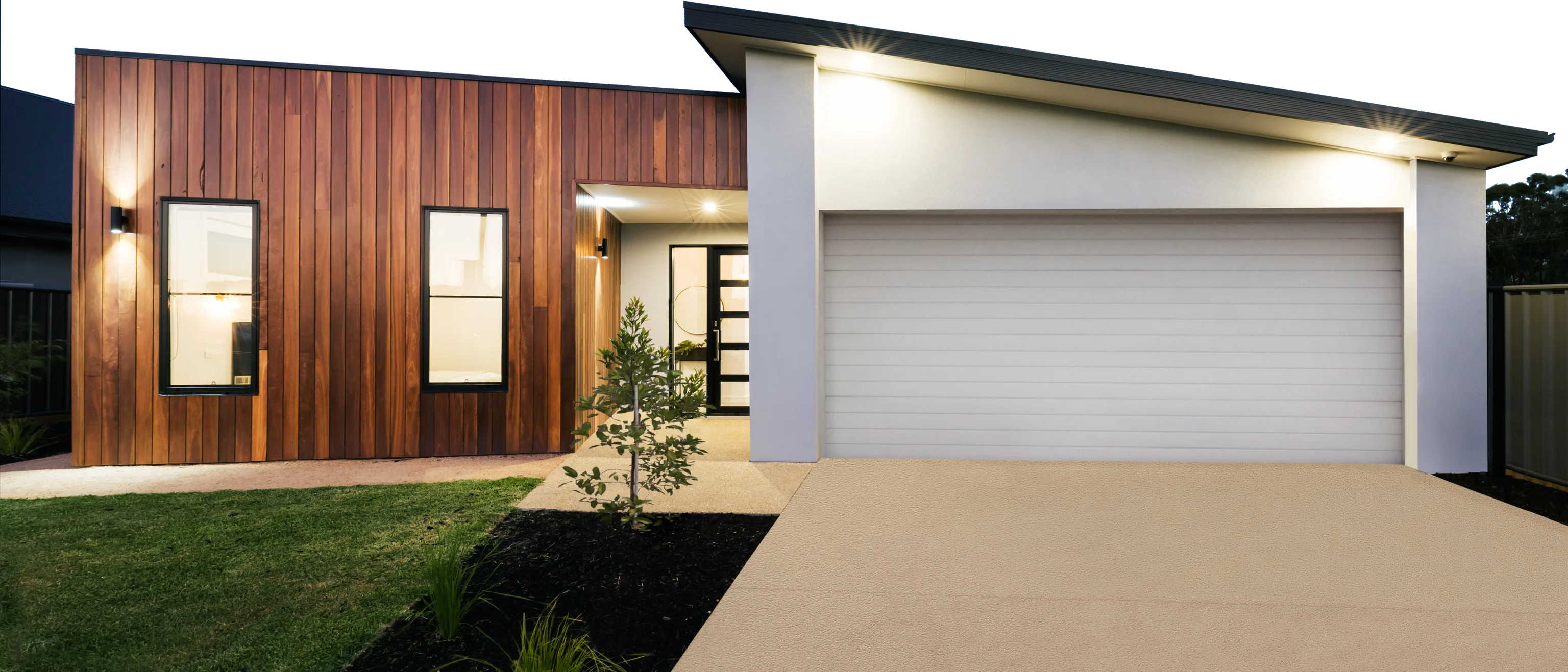 Modern home with timber cladding and a double garage lit at dusk