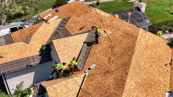 Aerial view of a roofing crew in high-visibility vests installing new roof decking on a home