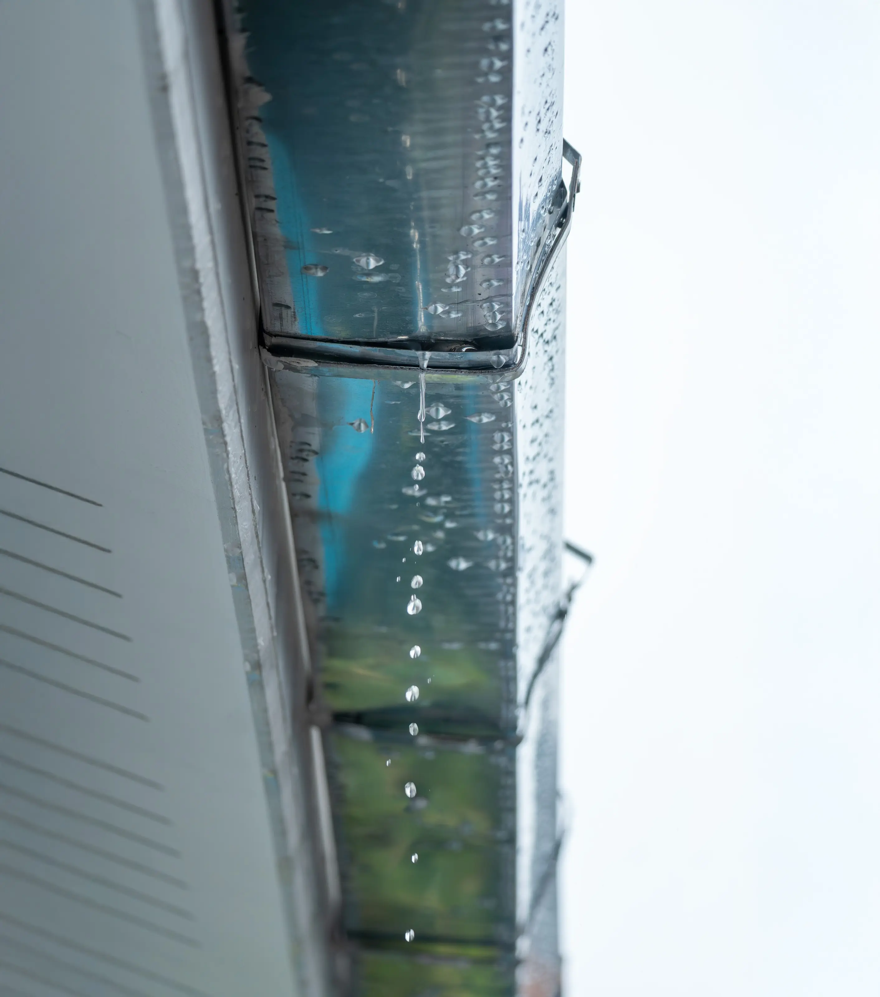 Rainwater overflowing a metal gutter on a commercial building, seen from below
