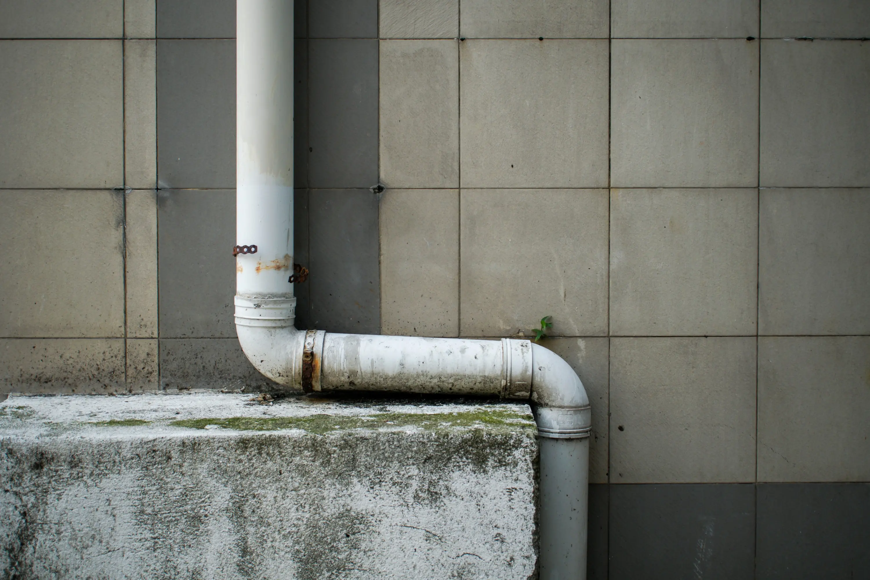 Weathered downspout bending around a concrete ledge on a commercial building