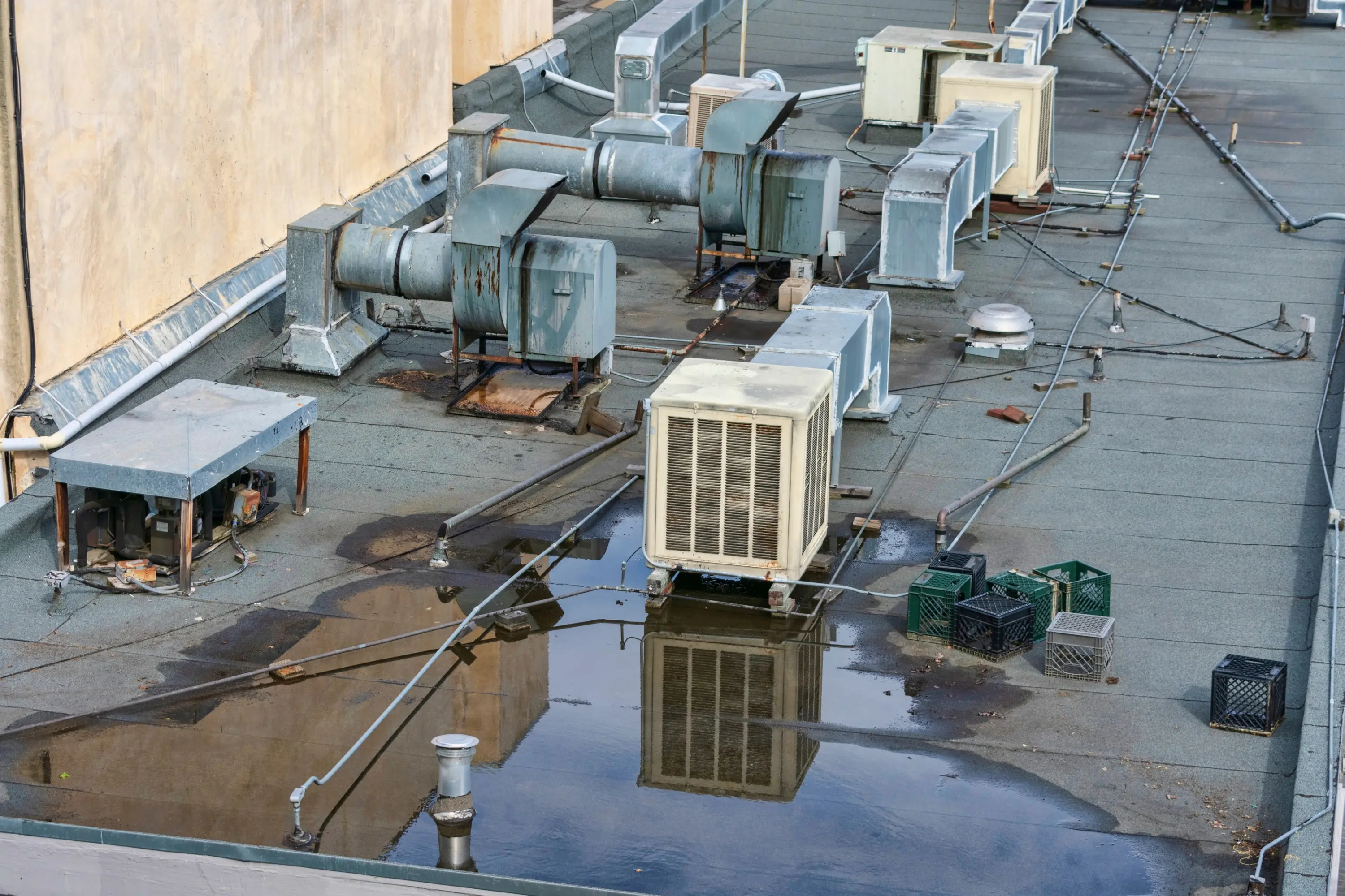 Ponding water around rooftop HVAC units on an ageing commercial flat roof