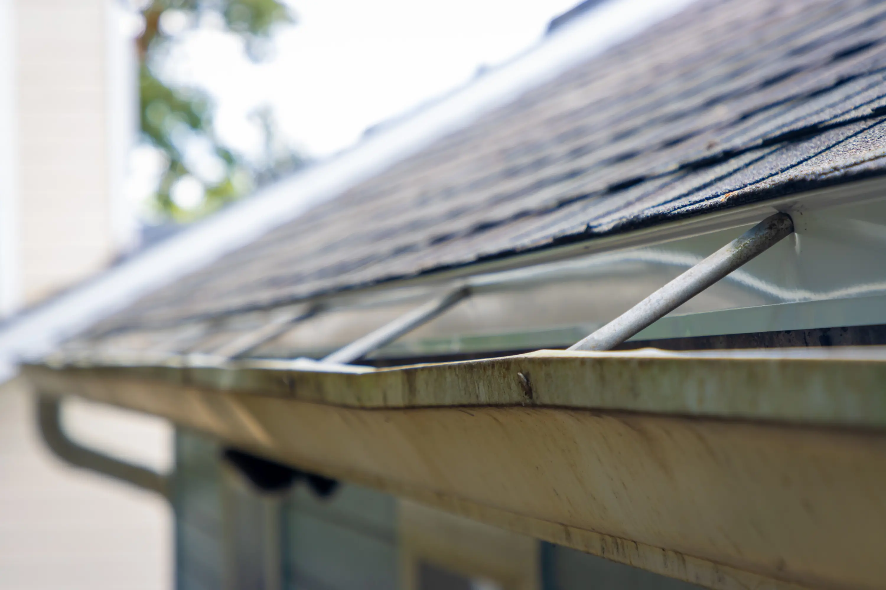 Close-up of a worn, dirty gutter with bent hangers along a shingle roof