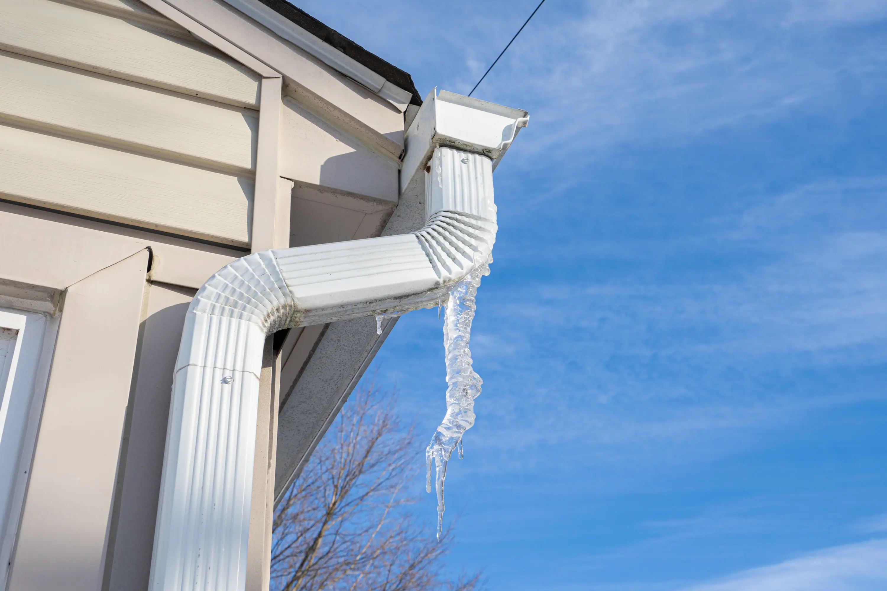 Downspout with an icicle hanging from the gutter outlet of a house