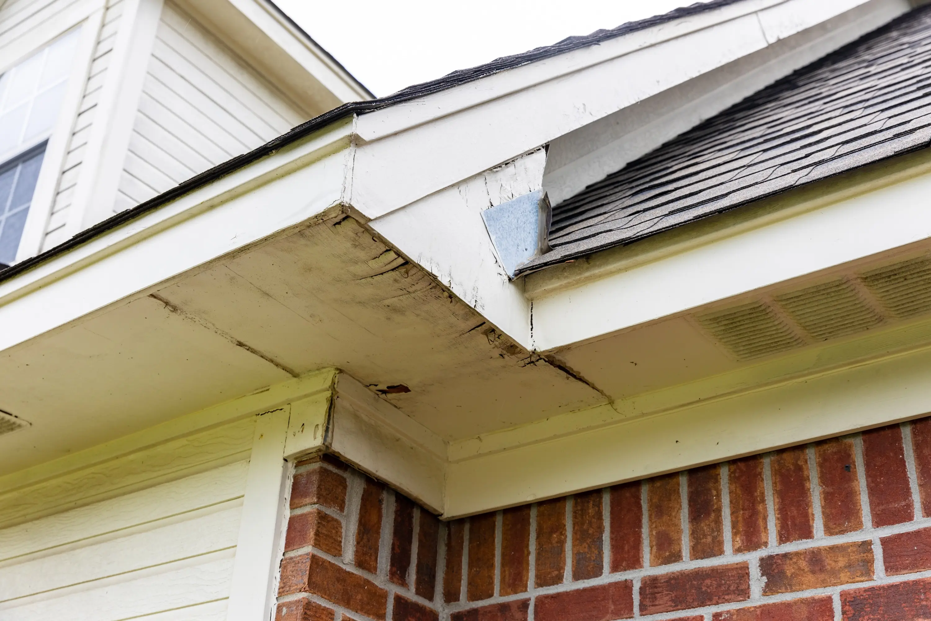 Water-stained fascia and soffit at a roof corner of a brick house