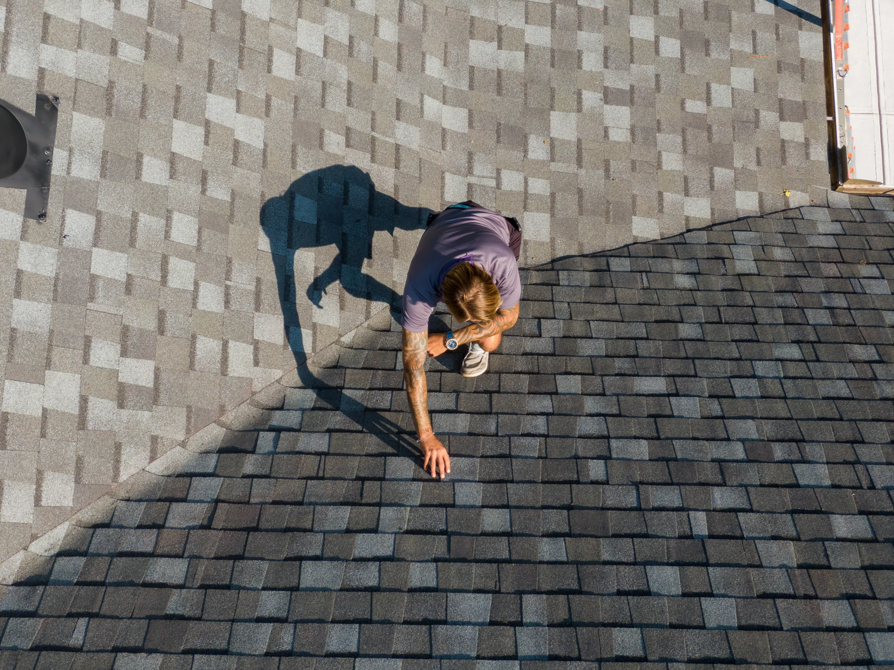 Roofer inspecting asphalt shingles on a residential roof, seen from above