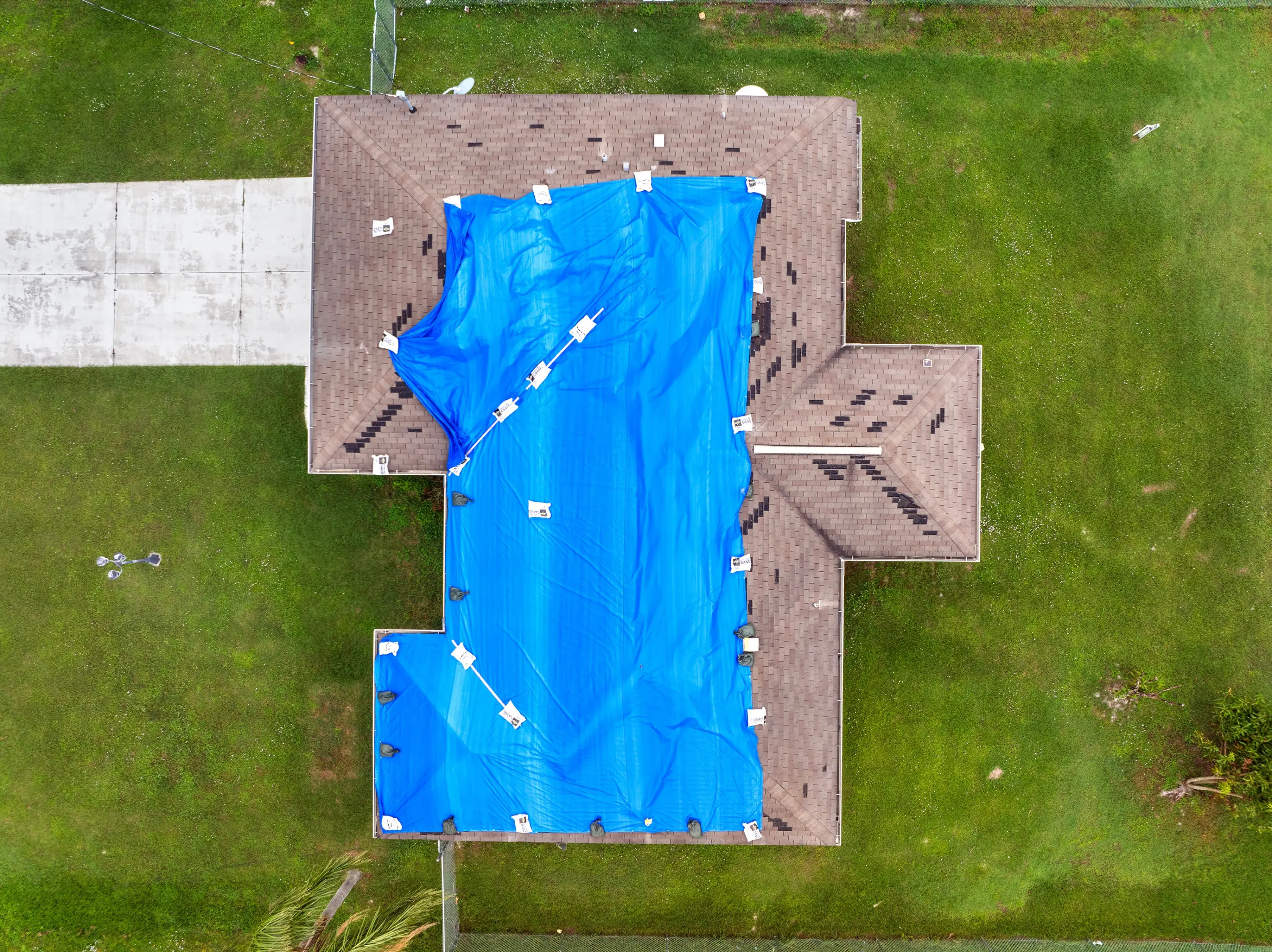 Aerial view of a house with a blue tarp covering storm damage on the roof