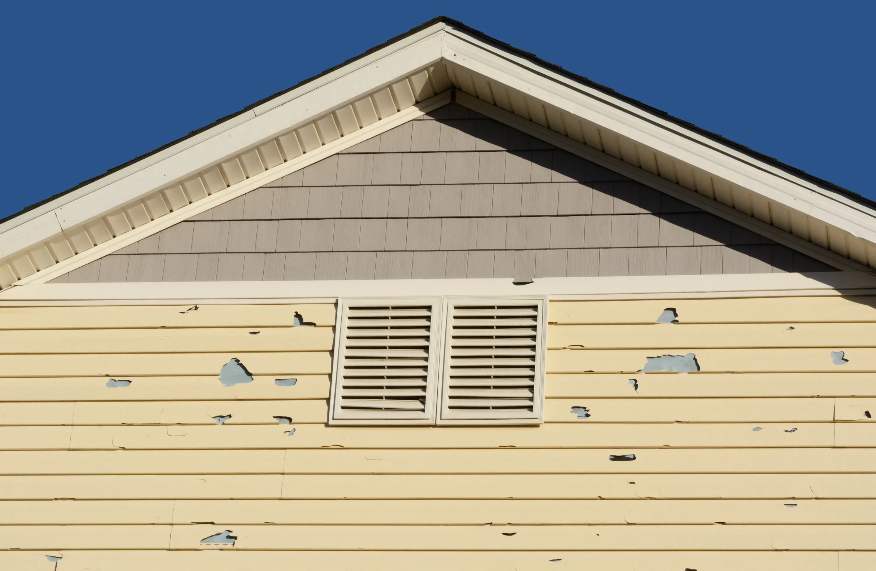Yellow lap siding with hail holes below a gable vent
